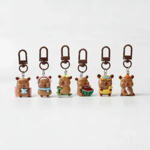 Set of 6 resin capybara bag charms lined up, featuring designs of capybaras reading, wearing a scarf, riding a scooter, eating watermelon, swimming with a floatie, and holding a fish.