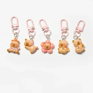 A set of five cute resin capybara bag charms featuring pink sakura cherry blossom themes, floral headbands, and pink metal lobster clasps on a white background.