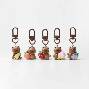 A collection of five cute resin capybara bag charms arranged in a row, each holding a different colorful fruit including a pear, persimmon, strawberry, peach, and mangosteen.