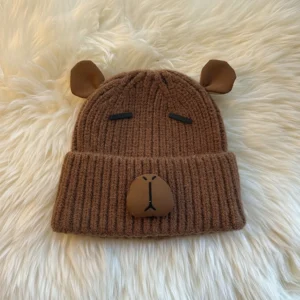 Camel ribbed knit cuffed beanie with a capybara face patch and small 3D ears on top.