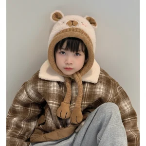 Child modeling a fluffy cream capybara beanie with a brown knitted brim and long earflaps ending in plush paws.