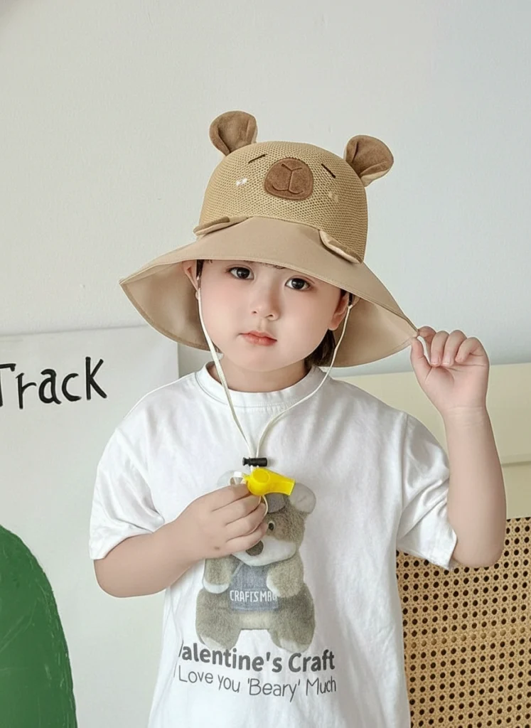 Child wearing a beige wide-brim sun hat with a breathable mesh crown, capybara face design, and a yellow safety whistle attached to the chin strap