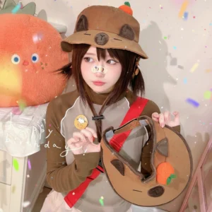 Model wearing a brown soft bucket hat with a 3D orange on top, next to a matching open-top visor style featuring the same cute capybara face and fruit detail.