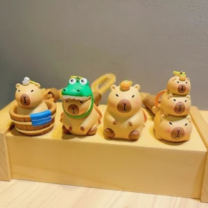 Four cute 3D PVC capybara keychains displayed on a wooden stand, featuring designs of a capybara in a bathtub, wearing a crocodile hat, balancing an orange, and a stack of three capybaras.