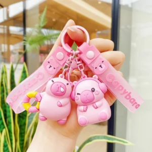 Pink PVC capybara keychain and bag charm featuring two styles: one with headphones and one with a swim ring, both with pink straps and alloy clasps.