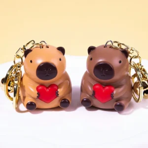 Two cute PVC capybara keychains in light and dark brown sitting and holding red light-up hearts with gold alloy clasps.