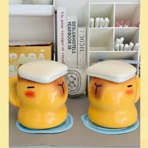 Yellow ceramic capybara cup shaped like a capybara taking a bath with a white towel-shaped lid and cute sleeping face.
