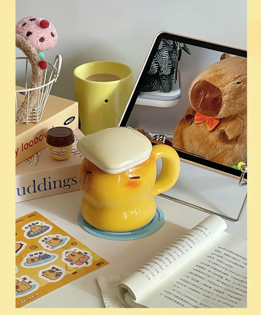 Yellow ceramic capybara cup shaped like a capybara taking a bath with a white towel-shaped lid and cute sleeping face.