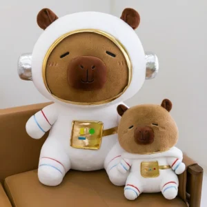 A large and a small astronaut capybara plush toy sitting on a brown chair, wearing white space suits with gold helmet visors and silver headset details.