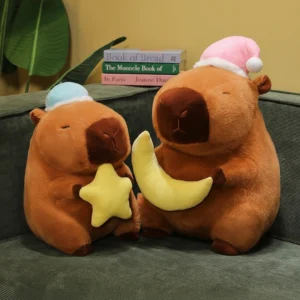 Two sleepy capybara plush toys sitting side by side; one wears a blue nightcap holding a yellow star, and the other wears a pink nightcap holding a yellow moon.