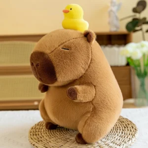 A soft brown capybara plush sitting upright with closed eyes and a small yellow duck toy perched on top of its head.