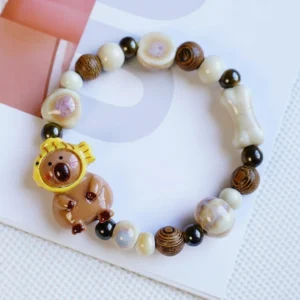 Beaded elastic bracelet featuring a capybara charm wearing a yellow Taiyaki fish hood, strung with brown wood-grain and cream ceramic beads.