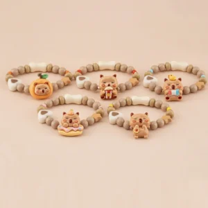 Group collection of five elastic beaded bracelets for kids featuring shiny capybara charms with popcorn, donut, sunflower, and fruit themes on a beige background.