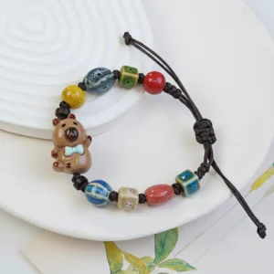 Close-up of two adjustable woven bracelets featuring glazed ceramic capybara charms in brown and beige tones.