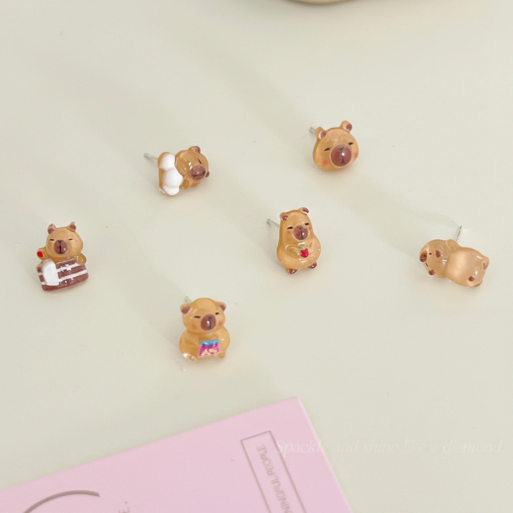 A collection of six pairs of mini capybara stud earrings featuring a capybara sleeping, wearing pajamas, bathing, and eating snacks.