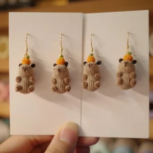 Custom handmade crochet capybara earrings featuring two designs: one with a tiny orange on its head and another with a red Santa hat.