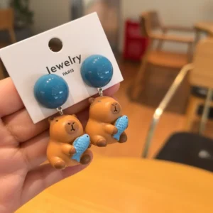 A pair of adorable 3D capybara stud earrings featuring a brown capybara hugging a bright orange fish, available in silver needles and clip-ons.