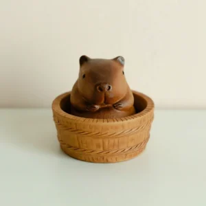 A brown textured purple clay capybara mini figure with a white towel on its head, resting in a tea bowl as a traditional Zisha tea pet.