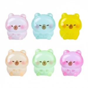 Six tiny capybara figures in different colors including pink, blue, and green, shown both in daylight and glowing with a green light in the dark.