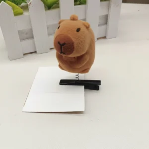 Close-up of a fuzzy flocked capybara figure mounted on a metal spring and black hair clip, shown from a side angle to highlight the bobble mechanism.