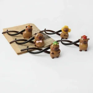 A collection of five 11cm twisted 5-shape hair clips in dark brown plastic, featuring 3D capybara charms with accessories like a red hat, turtle, and fish hood.