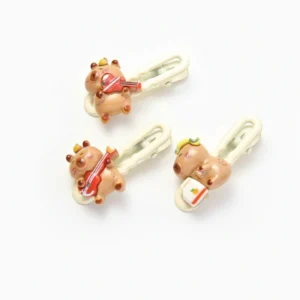 A side-by-side view of three 3D resin capybara hair clips: one playing a violin, one playing a guitar, and one wearing headphones holding a radio.