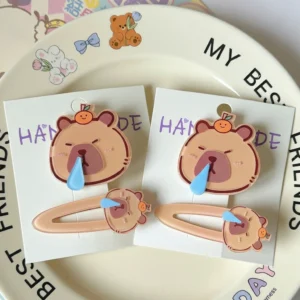 Close-up of a glossy acrylic capybara hair clip featuring a sleeping face with a blue snot bubble and a small orange on its head.