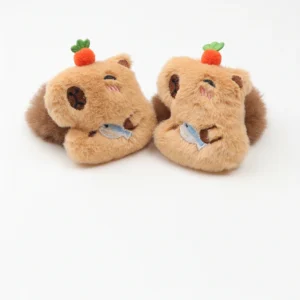 Close-up of a brown plush capybara hair scrunchie featuring a winking face, a carrot on its head, and holding a small blue fish.
