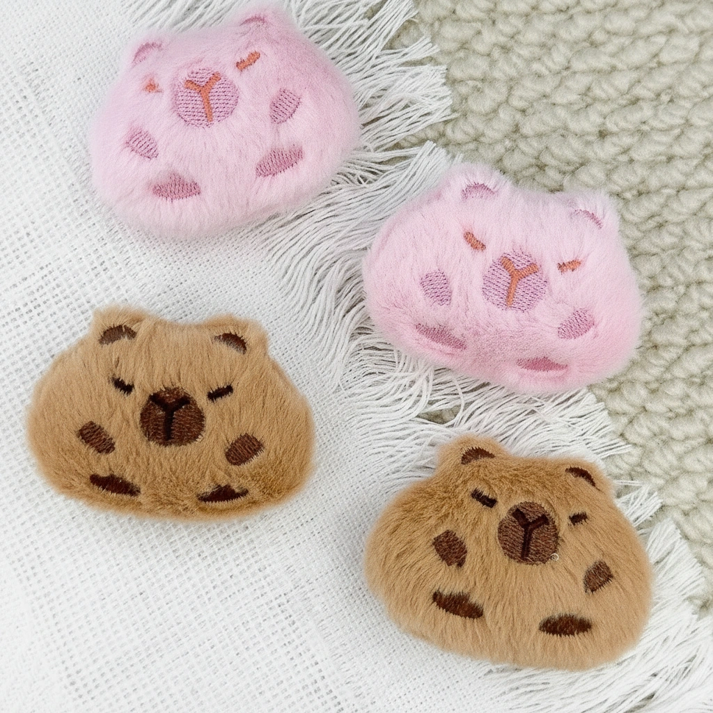 Close-up of a soft, fuzzy capybara head brooch in brown and pink colors, featuring embroidered facial details and a plush texture.
