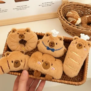 A collection of six bakery-themed plush pins shaped like a croissant, baguette, donut, fried chicken leg, bread loaf, and a chef bun, all featuring embroidered capybara faces.