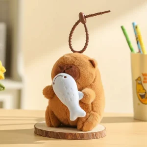 A 12cm interactive capybara plush keychain holding a Sacabambaspis fish, shown hanging from a bag with a pull-string mechanism that makes it shake.
