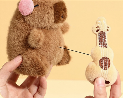 Hand pulling the plush guitar instrument away from the capybara's body to show the retractable black string.