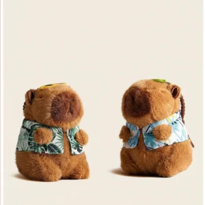 Two capybara plush keychains sitting side-by-side, one wearing a green Hawaiian shirt and one wearing a blue Hawaiian shirt, both with yellow sunglasses on their heads.