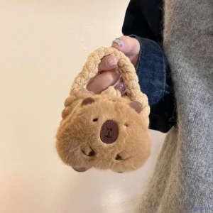 A fuzzy, beige mini handbag shaped like a capybara head, featuring soft twisted handles and a plush texture, held by a model.