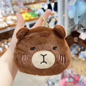 Fuzzy plush capybara head coin purses in dark brown, featuring embroidered sleeping faces and gold keychain clips.